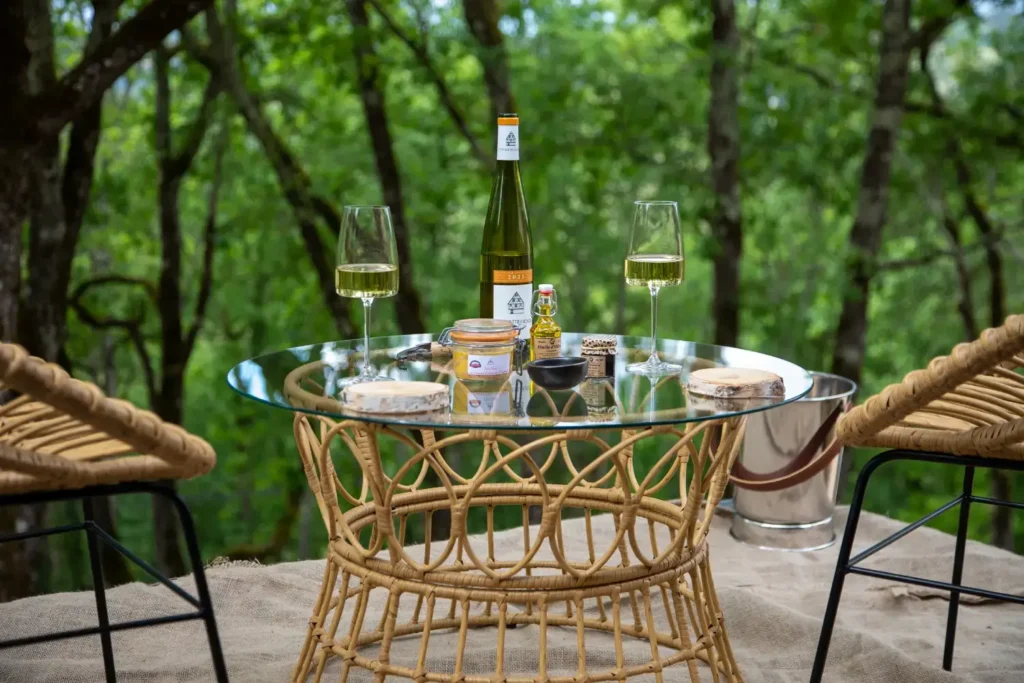 WYN Wine Bar outdoor tasting setup with white wine, gourmet treats, and rattan chairs on a forest-view terrace at La Perle de Domme in Dordogne.