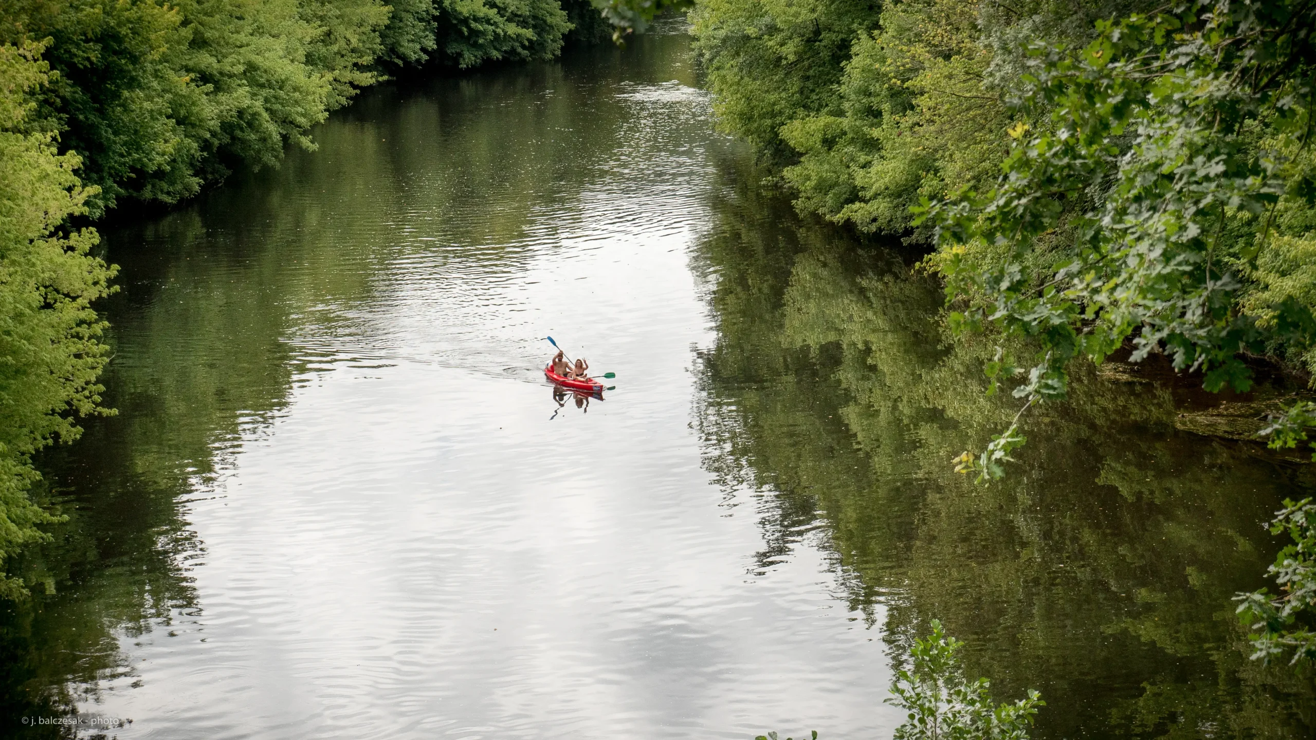 A top-down view of two people in a red kayak canoeing on the Dordogne River.