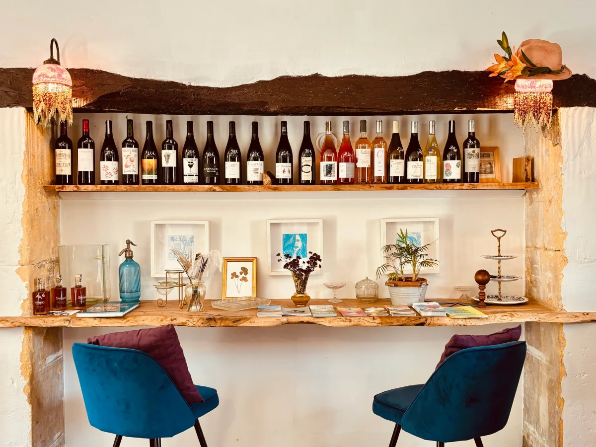Interior view of Restaurant DÔMA, one of the best restaurants in Domme, showcasing a rustic wine display on a wooden shelf above a bar area with two blue velvet chairs.