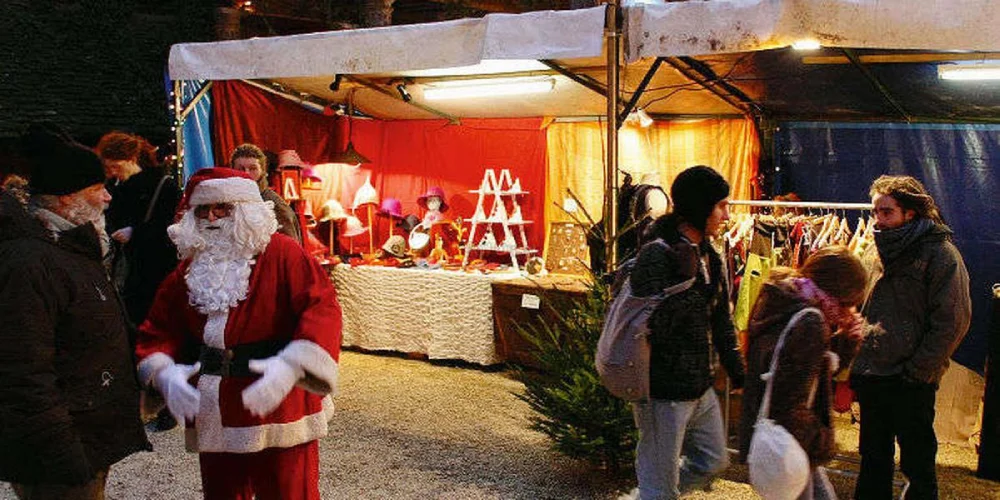 Santa Claus and shoppers at a stall illuminated at night in Bergerac Christmas Market, one of the Christmas markets in Dordogne.