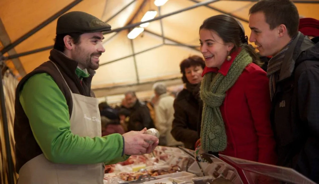 A local vendor presenting a gourmet item to customers at one of the Christmas markets in Dordogne.