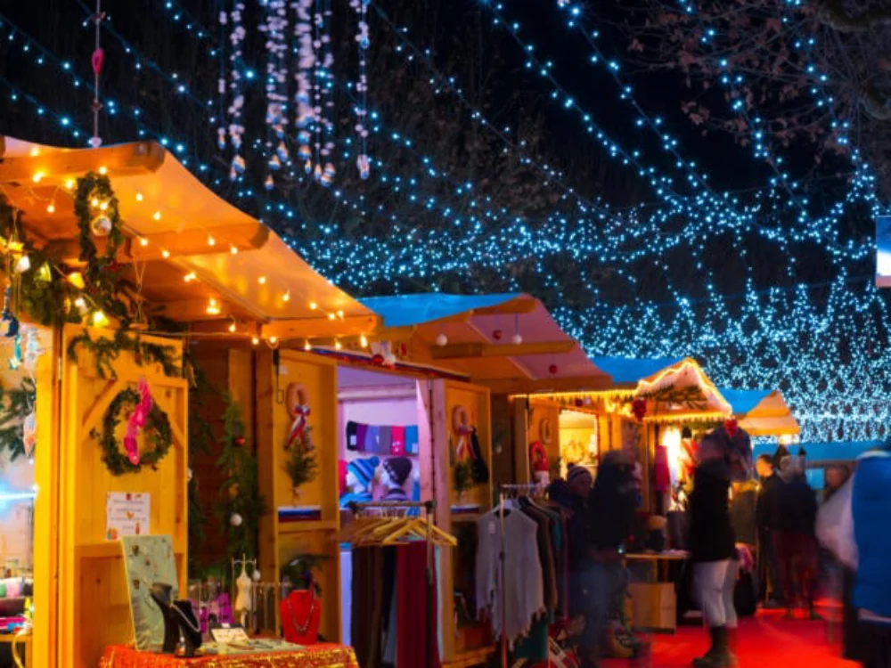 Wooden chalet stalls brightly lit with warm lights under a canopy of blue string lights at Sarlat, one of the Christmas markets in Dordogne.
